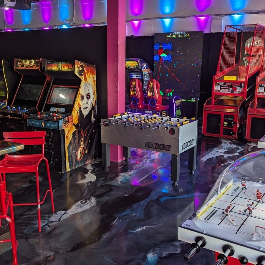 The arcade floor at The Circuit: cabinets, foosball and air hockey under magenta and blue lights